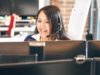 A women infront of a screen, wearing a headset while smiling