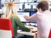 Two coworkers sitting at a desk, one of them pointing on the screen